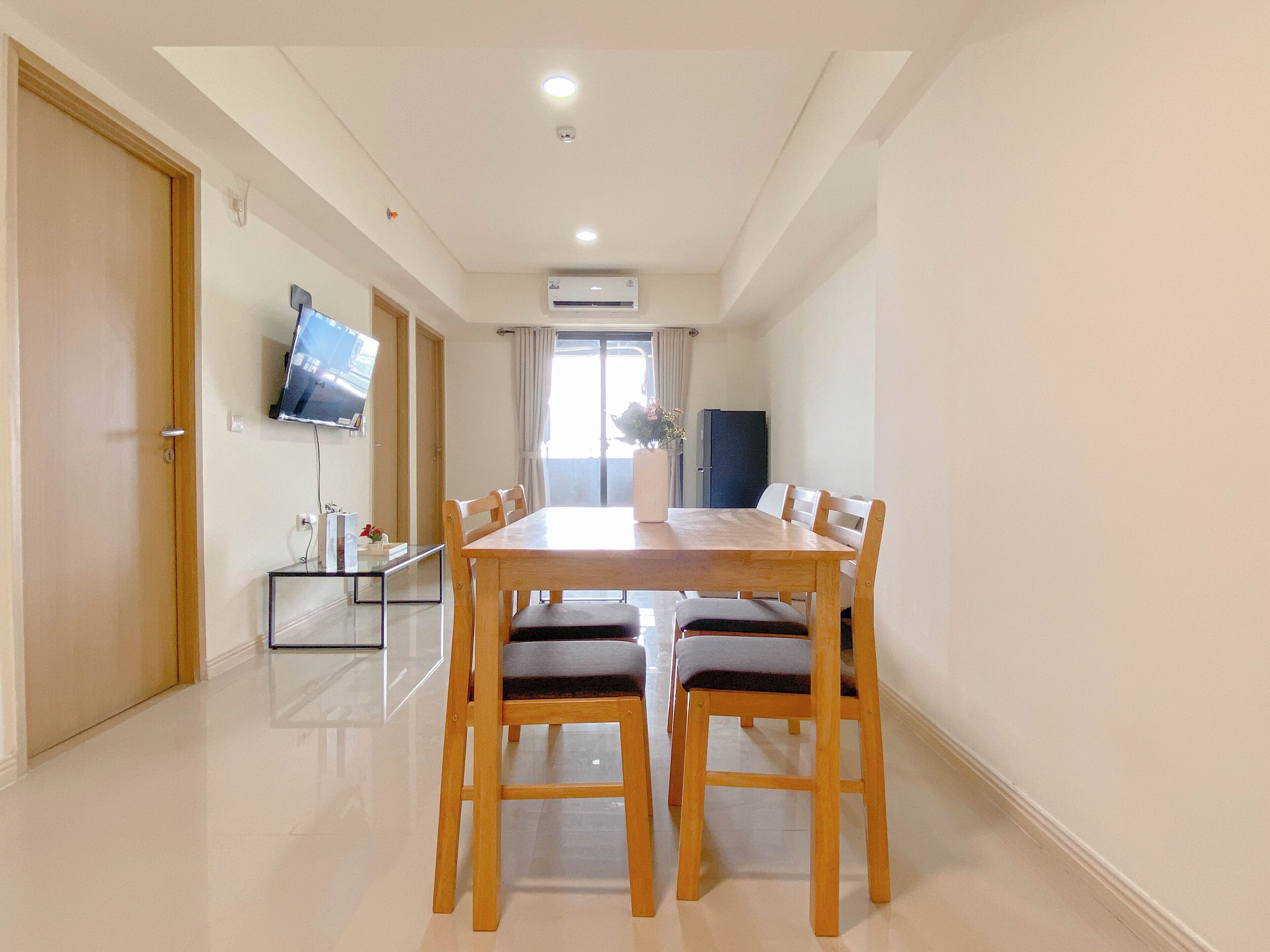 A dining area with a wooden table and chairs, a TV mounted on the wall, and an air conditioning unit above the door.
