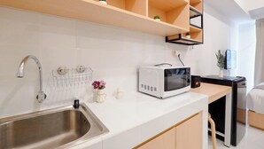 A modern kitchen with a stainless steel sink, a microwave, and wooden shelves above the counter. - Basic Look Studio (No Kitchen) Apartment Tokyo Riverside Pik 2 (Teluknaga)