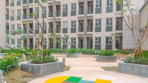 A multi-story residential building with balconies, surrounded by landscaped areas with planters and trees. - Simple 2Br With Extra Room Transpark Juanda Bekasi Timur Apartment (Bekasi)