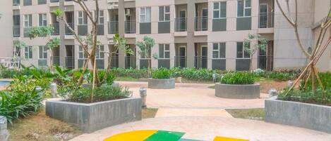 A multi-story residential building with balconies, surrounded by landscaped areas with planters and trees.