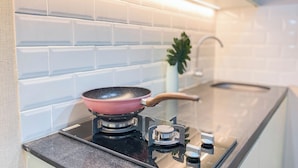 A kitchen with a gas stove, a pink frying pan, and a small plant on the counter. - Simple 2Br With Extra Room Transpark Juanda Bekasi Timur Apartment (Bekasi)