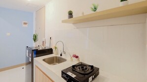 A modern kitchen with a sink, a stove, and a refrigerator. There are small plants on a shelf above the sink.
