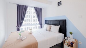 A modern hotel room with a large bed, a bedside table with a plant, and a view of buildings through the window.