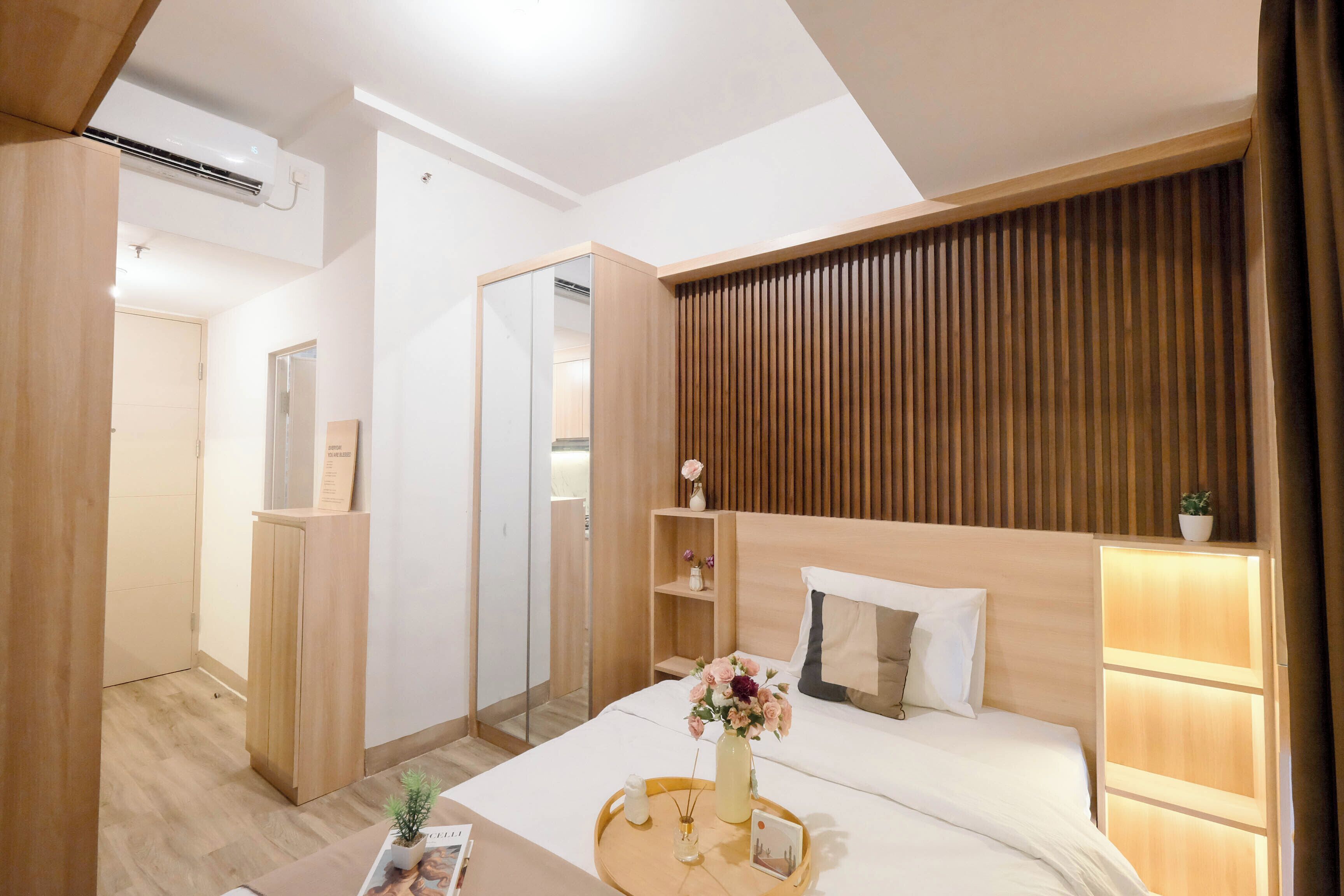 Una camera d'albergo moderna con una testiera in legno, un comodino con un vassoio, uno specchio e un armadio.