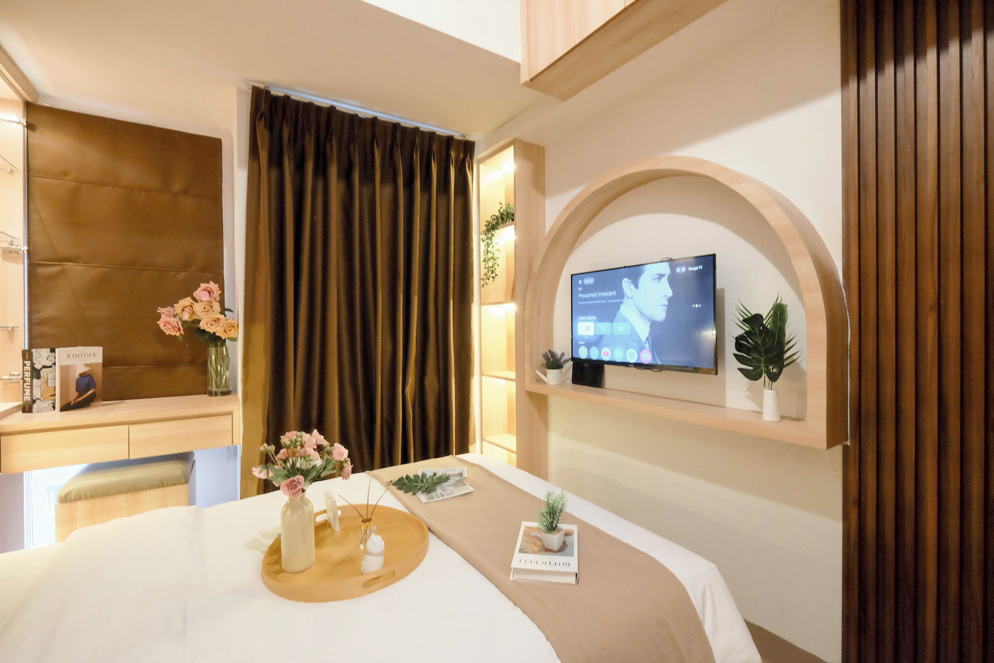 A hotel room with a bed, a desk, a television mounted on the wall, and a window with curtains.