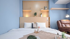 A neatly arranged bedroom with a bed, a brown leather chair, a bedside table with a lamp, and a wall-mounted shelf with decorative items.