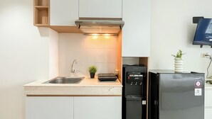 A compact kitchen with a stainless steel sink, a built-in range hood, a black refrigerator, and a small potted plant.