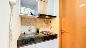 A kitchen with a sink, a stove, a plant, and a cabinet. - Wooden Nest 2Br Without Living Room At Evenciio Margonda Apartment (Depok)