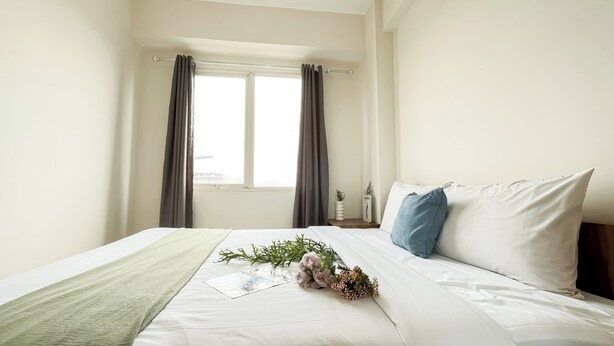 Ein ordentlich bezogenes Bett mit weißen Leinen, einer grünen Tagesdecke und einer Blumenkomposition.