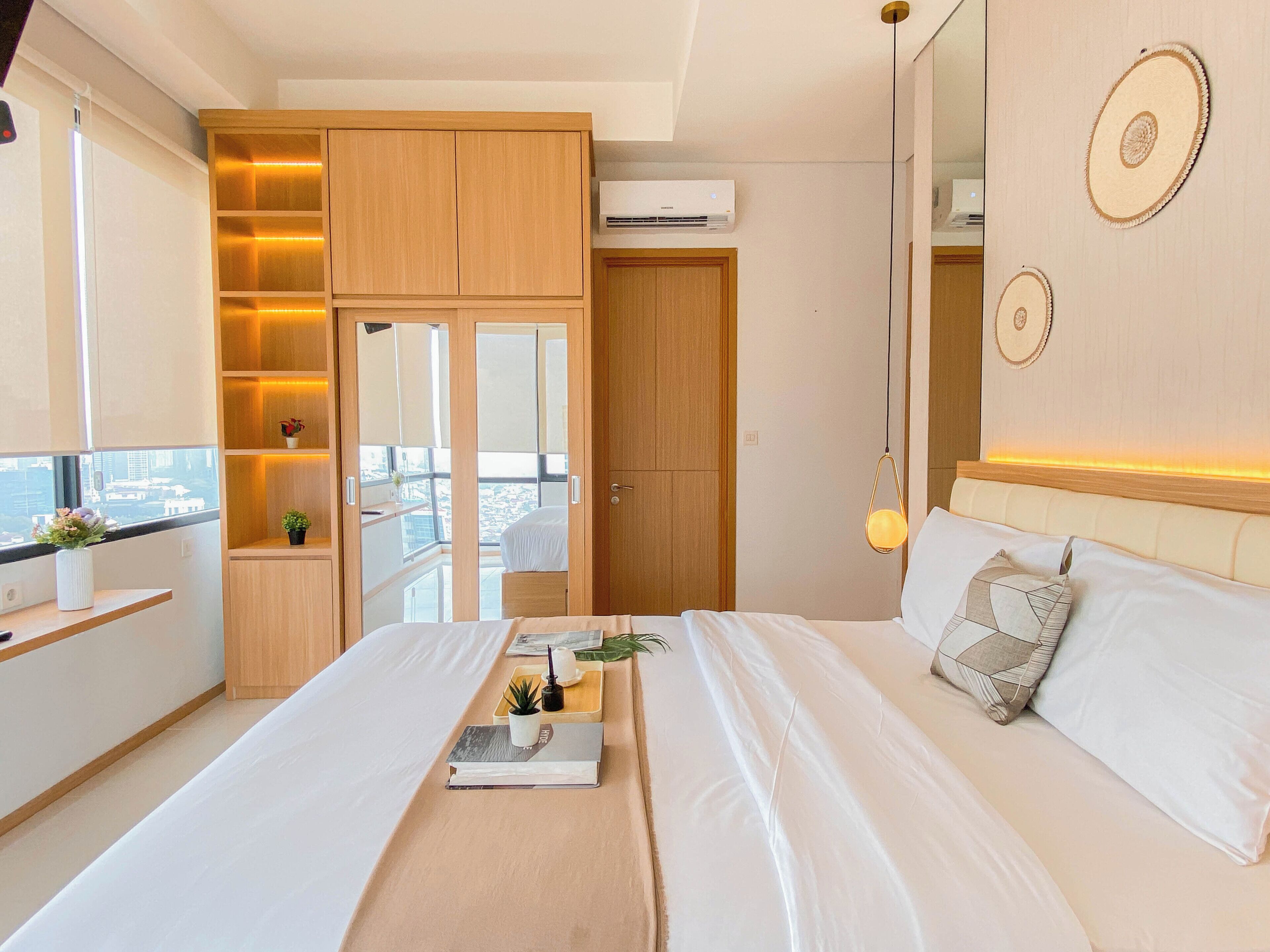A modern bedroom with a bed, bedside table, and a view of the city through a large window.