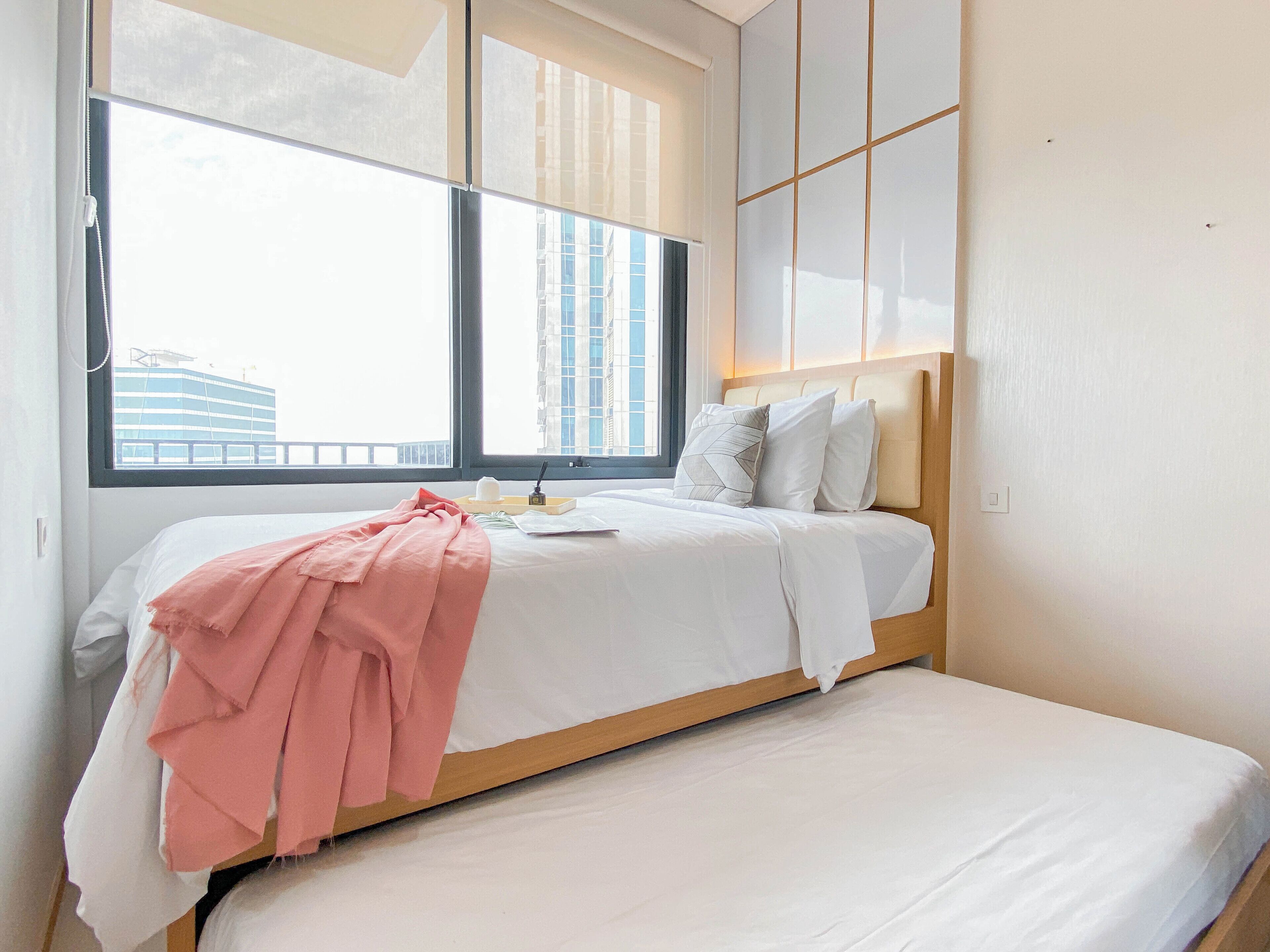A modern bedroom with a bed, a bedside table, and a window with a view of buildings.