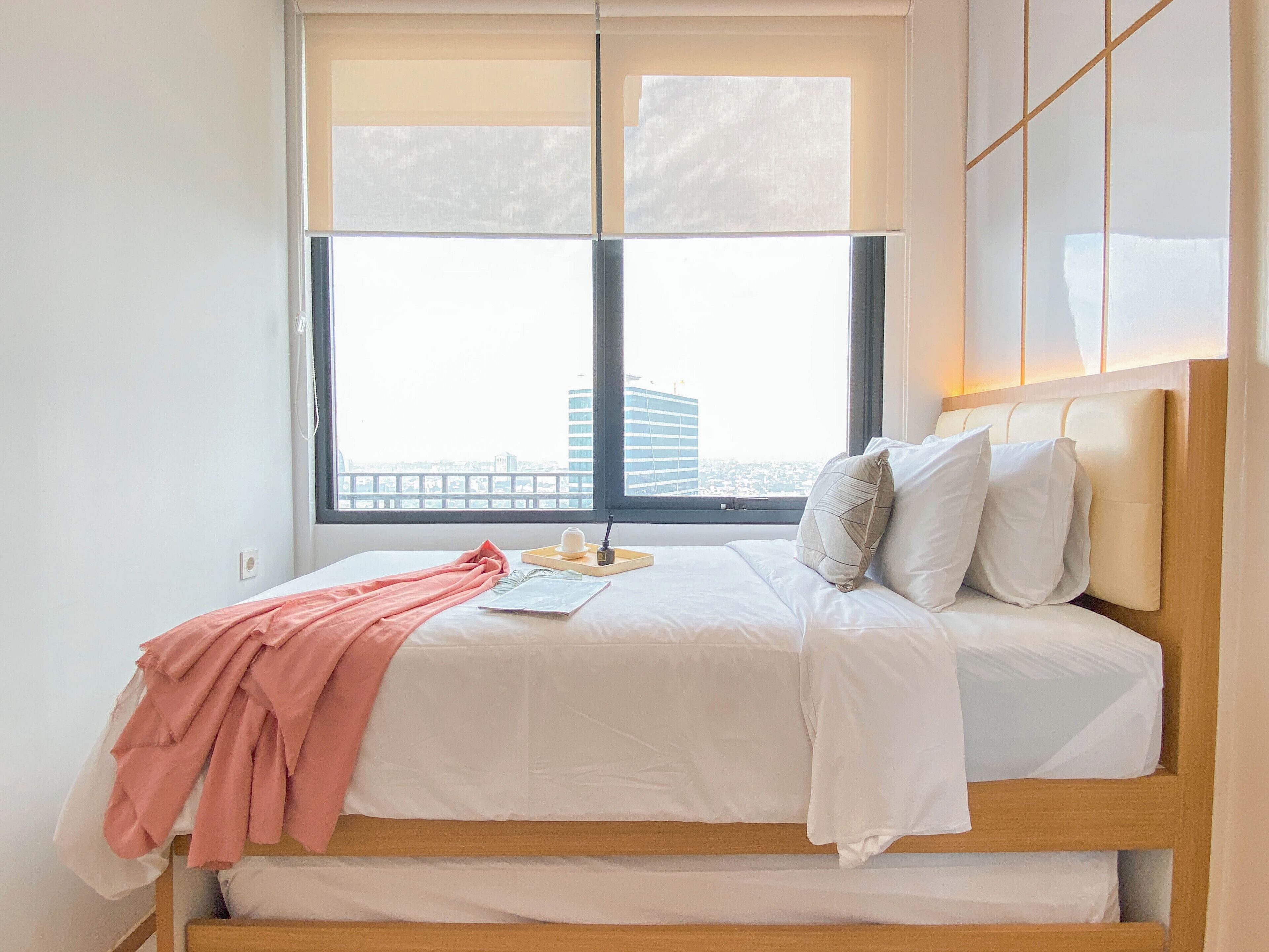 A neatly made bed with white linens, a pink blanket, and a small bedside table with a book and a cup.