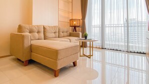 A modern living room with a beige sectional sofa, a small round table, and a floor lamp. - Warm Contemporary 2Br Apartment At Samara Suites (Jakarta)