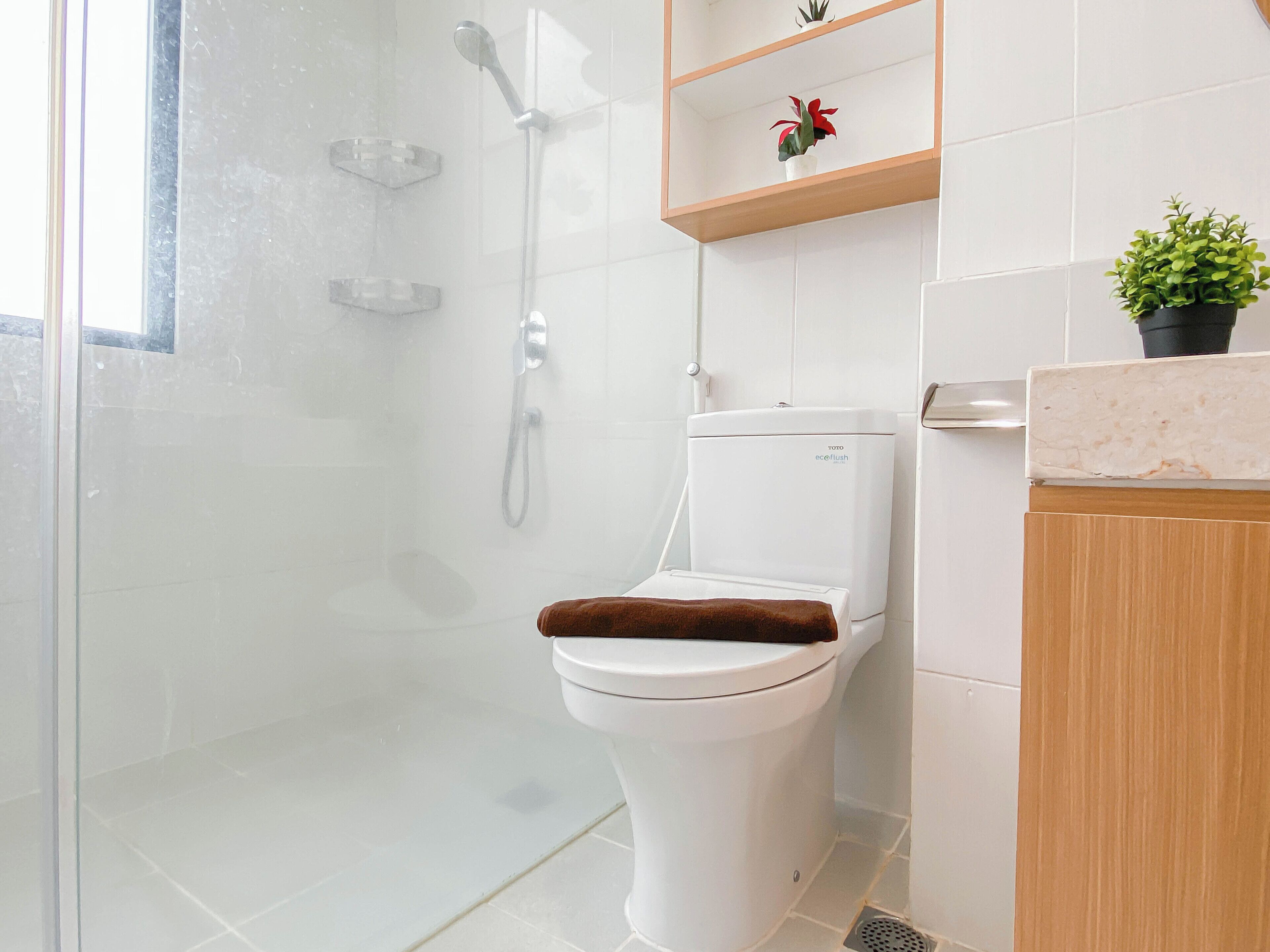 Un bagno moderno con doccia vetrata, un water Toto e uno scaffale in legno con una pianta in vaso.