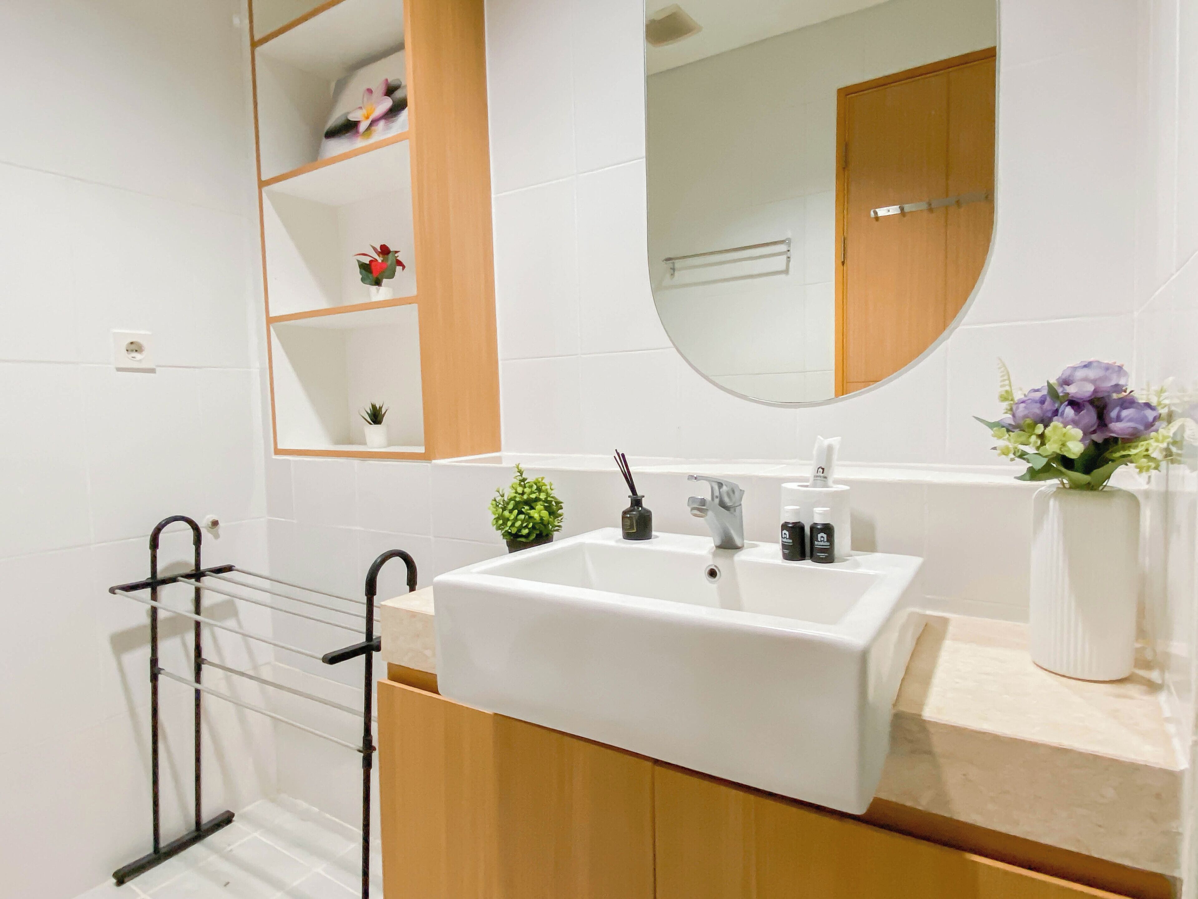 Un baño moderno con un lavamanos blanco, armarios de madera, un espejo y un perchero para toallas.