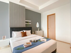 A modern hotel room with a large bed, bedside tables, a mirror, and a door. - Modern Monochromatic 2Br Near Lrt Station At Apartment Samara Suites (Jakarta)