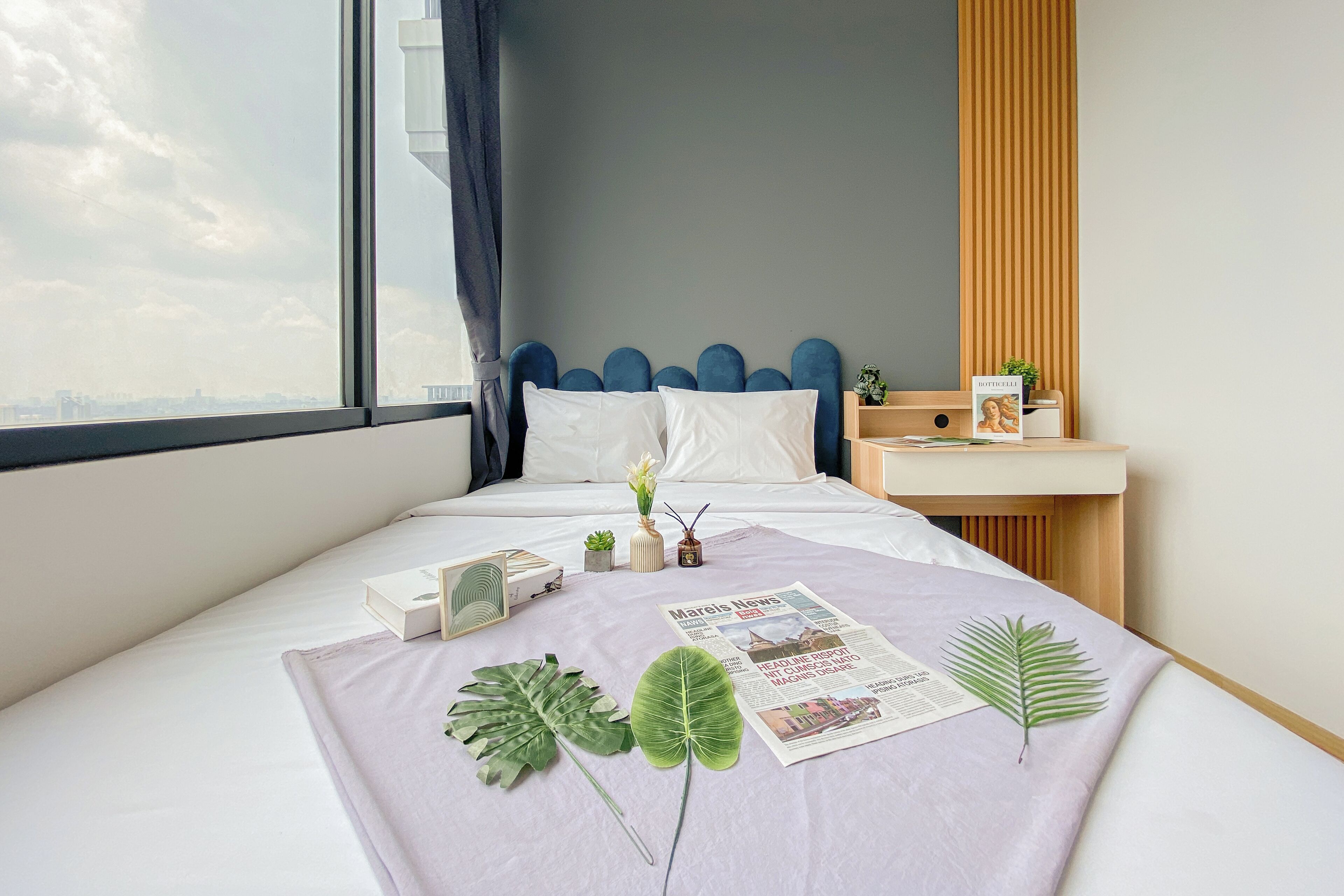 A neatly made bed with a magazine, a framed picture, and a plant on a bedspread.