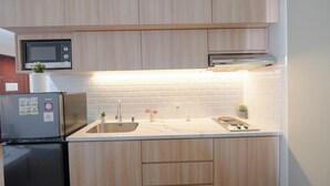 A modern kitchen with wooden cabinets, a stainless steel refrigerator, a microwave, a sink, and a stove. - Cozy And Spacious 1Br Apartment At Marina Ancol (Jakarta)