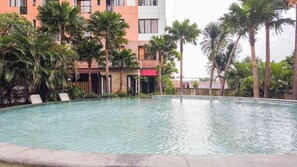 A swimming pool surrounded by palm trees and a building with balconies.