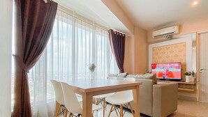 A modern living room with a dining table, white chairs, a sofa, and a TV. - Simple And Homey 2Br At Grand Kamala Lagoon Apartment (Bekasi)