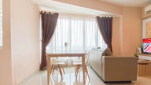 A modern living room with a dining table, white chairs, a sofa, and a TV. - Simple And Homey 2Br At Grand Kamala Lagoon Apartment (Bekasi)