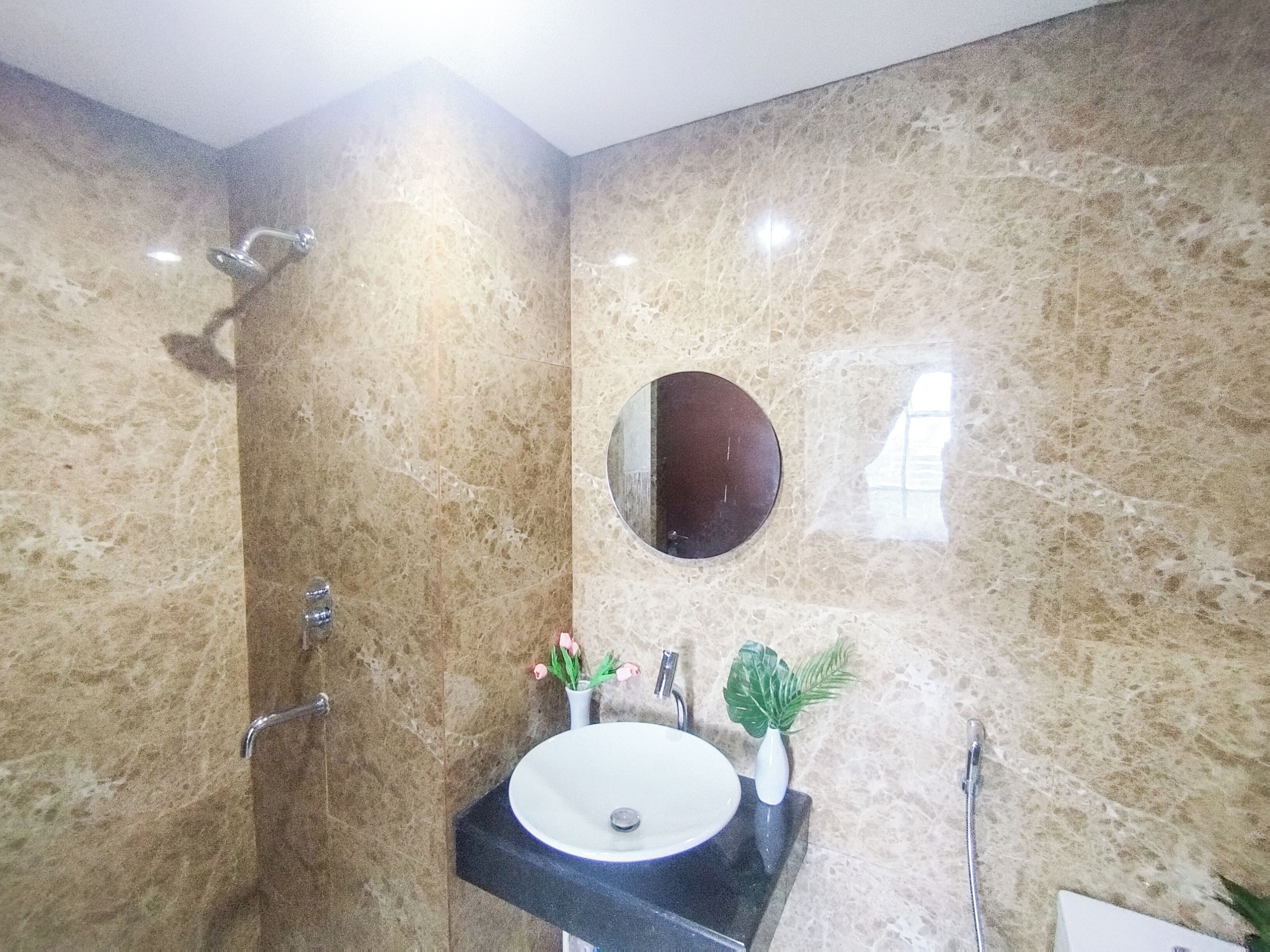 Un bagno con parete in marmo, uno specchio rotondo, un lavandino e una doccia.
