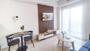 A modern living room with a dining area, a TV mounted on a wooden panel, a sofa, and a coffee table.