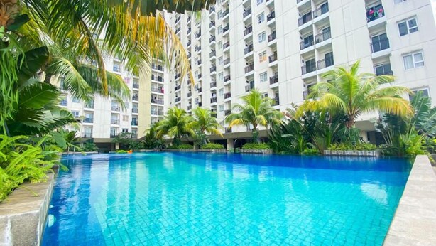 A swimming pool surrounded by lush greenery and a multi-story building with balconies. - Cozy Bloom Studio Apartment Cinere Resort (Depok)