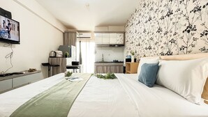 A hotel room with a bed, a desk, a kitchenette, and a bathroom. - Cozy Bloom Studio Apartment Cinere Resort (Depok)