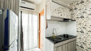 A compact kitchen with a built-in stove, a sink, and a window with sheer curtains. - Cozy Bloom Studio Apartment Cinere Resort (Depok)