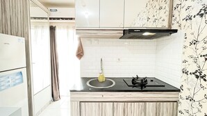 A compact kitchen with white cabinets, a gas stove, and a modern design. - Cozy Bloom Studio Apartment Cinere Resort (Depok)
