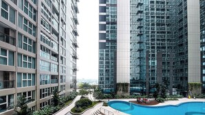 A modern residential building with a swimming pool, outdoor seating, and a view of the city. - Cozy Loft 2Br At Grand Jati Junction Apartment (Medan)