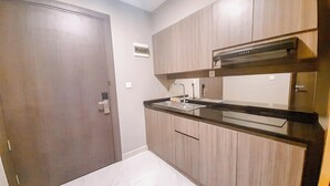 A compact kitchen with wooden cabinets, a black countertop, and a built-in microwave. - Cozy Loft 2Br At Grand Jati Junction Apartment (Medan)