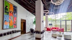 Un hall d’entrée moderne agrémenté d’une grande fresque colorée, d’un espace détente lumineux avec des canapés rouges et d’un mur de verre donnant sur un paysage verdoyant.