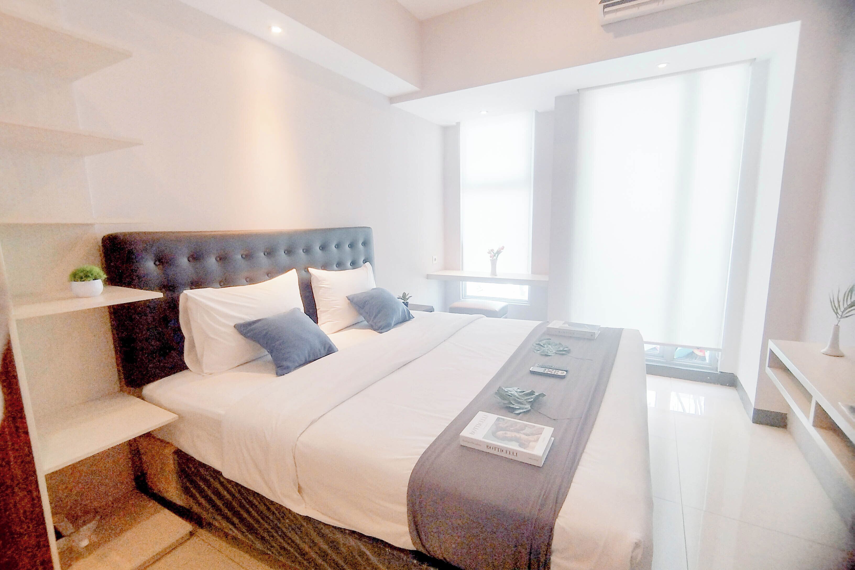 A modern bedroom with a large bed, a bedside table, a window, and a small plant.