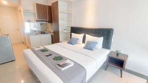 A modern hotel room with a large bed, bedside tables, a small kitchen area, and built-in shelving.