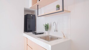 A modern kitchen with white tiles, a black refrigerator, a sink, and a countertop with a plant and a small vase. - Cozy And Spacious 2Br Apartment Tokyo Riverside Pik 2 (Teluknaga)