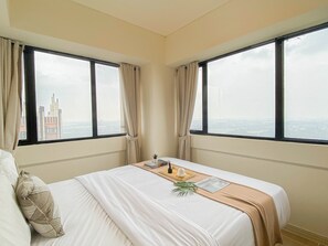 Ein Hotelzimmer mit einem großen Bett, zwei mit Vorhängen versehenen Fenstern, Blick auf eine Stadtlandschaft und einer kleinen Pflanze auf dem Bett.