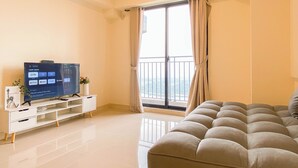 Een moderne woonkamer met een flatscreen-televisie, een bank, een balkon met gordijnen en een airconditioning.