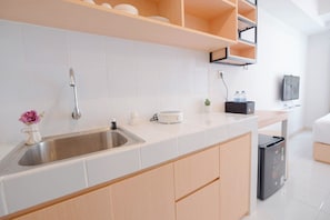 A modern kitchen with a stainless steel sink, white tiles, wooden cabinets, a built-in oven, and a small potted plant.