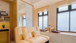 A modern living room with a sofa, a small table, and a large window offering a city view. - Japanese Style Studio At Pollux Chadstone Apartment (Cikarang)