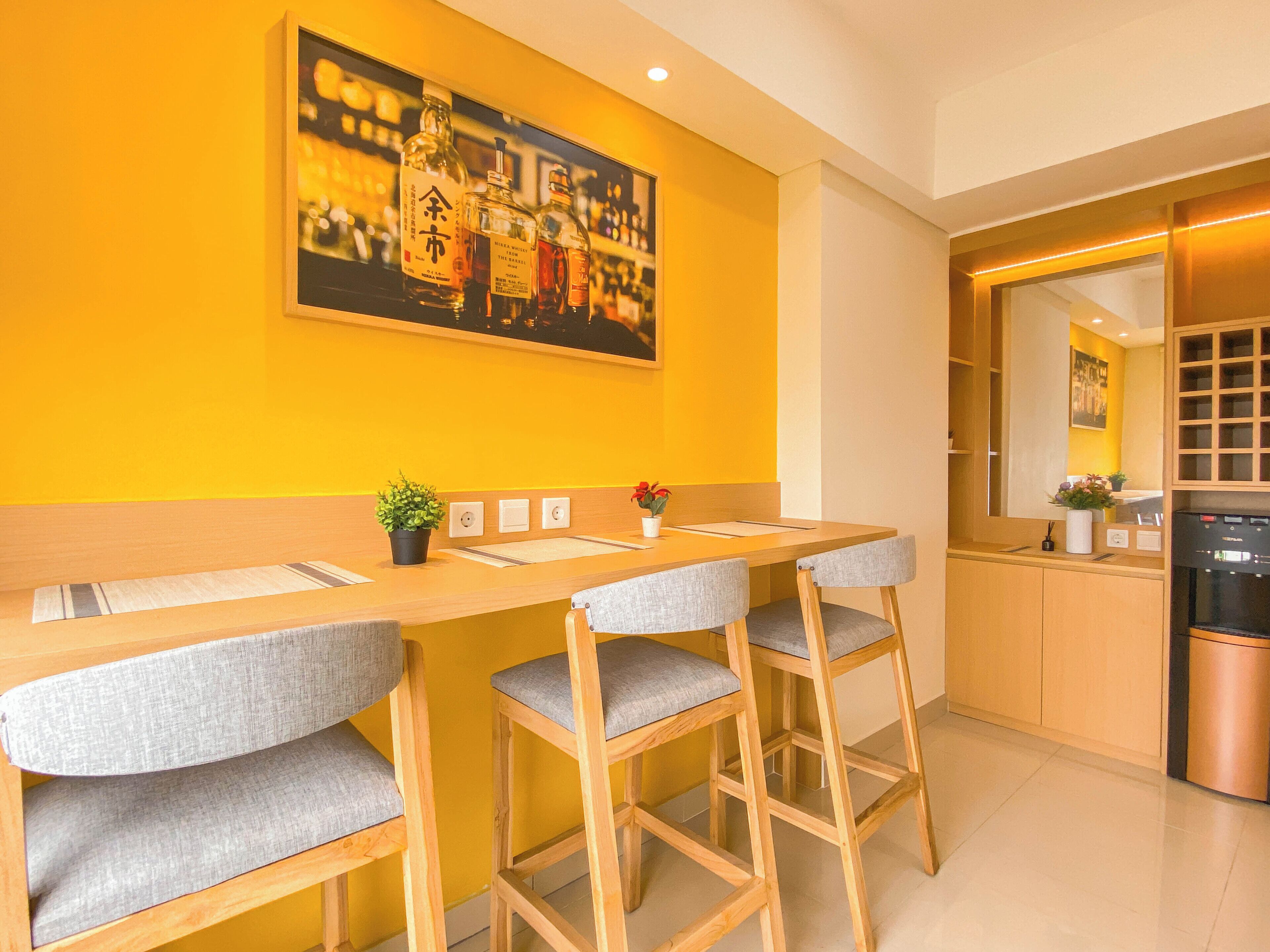 A modern kitchen with a yellow wall, wooden bar stools, a painting, and a built-in oven.
