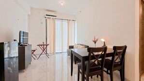 A modern living room with a dining area, a flat-screen TV, a small table with chairs, and a sofa. - Cozy And Pool View 2Br At Sky House Bsd Apartment (Pagedangan)