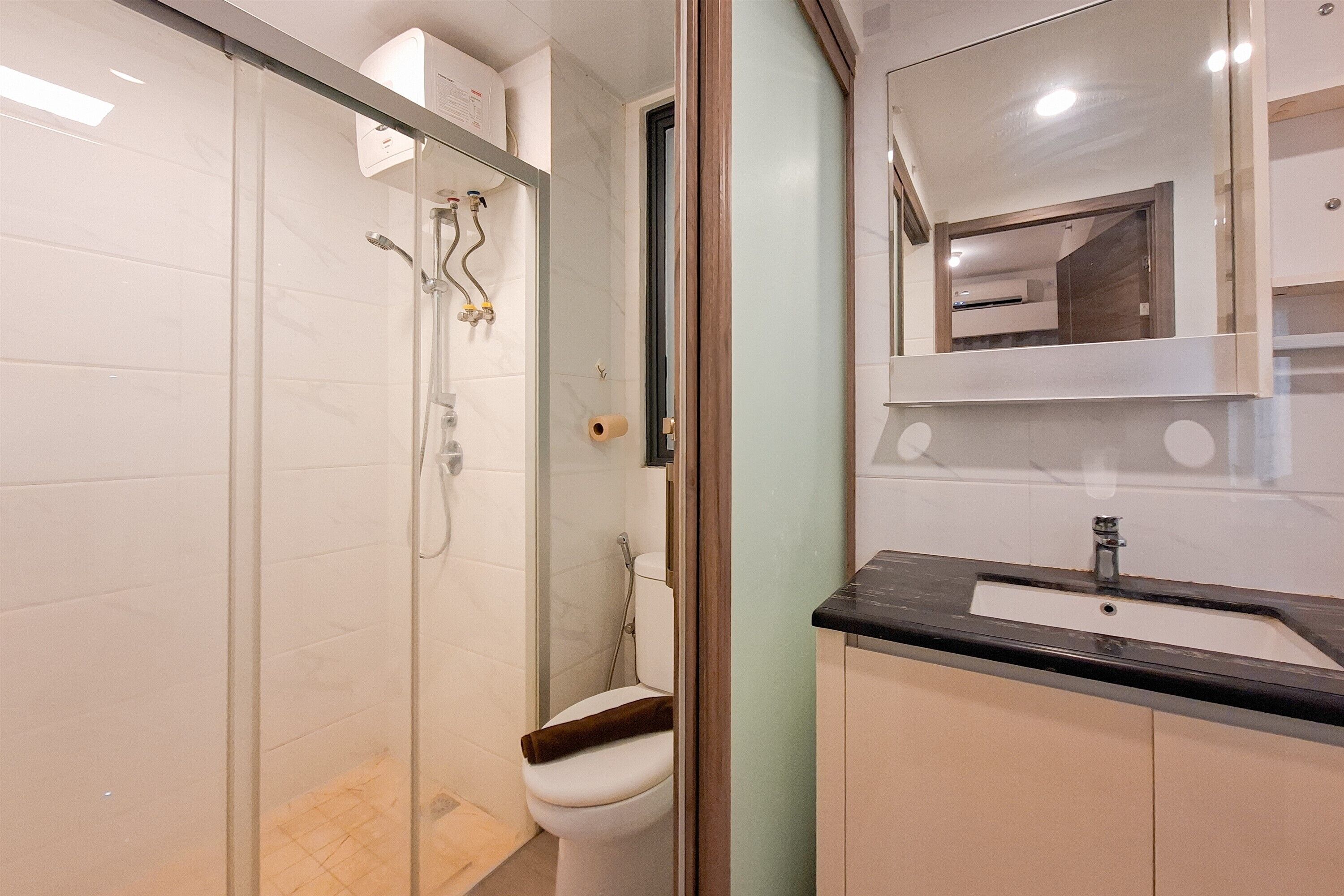 A bathroom with a glass-enclosed shower, a toilet, and a sink with a mirror above it.