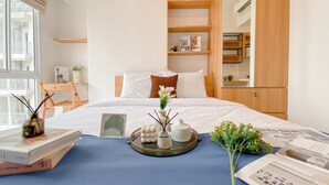 Una habitación de hotel moderna con una cama grande, una mesita de noche con libros, una bandeja con adornos y vistas al balcón exterior.