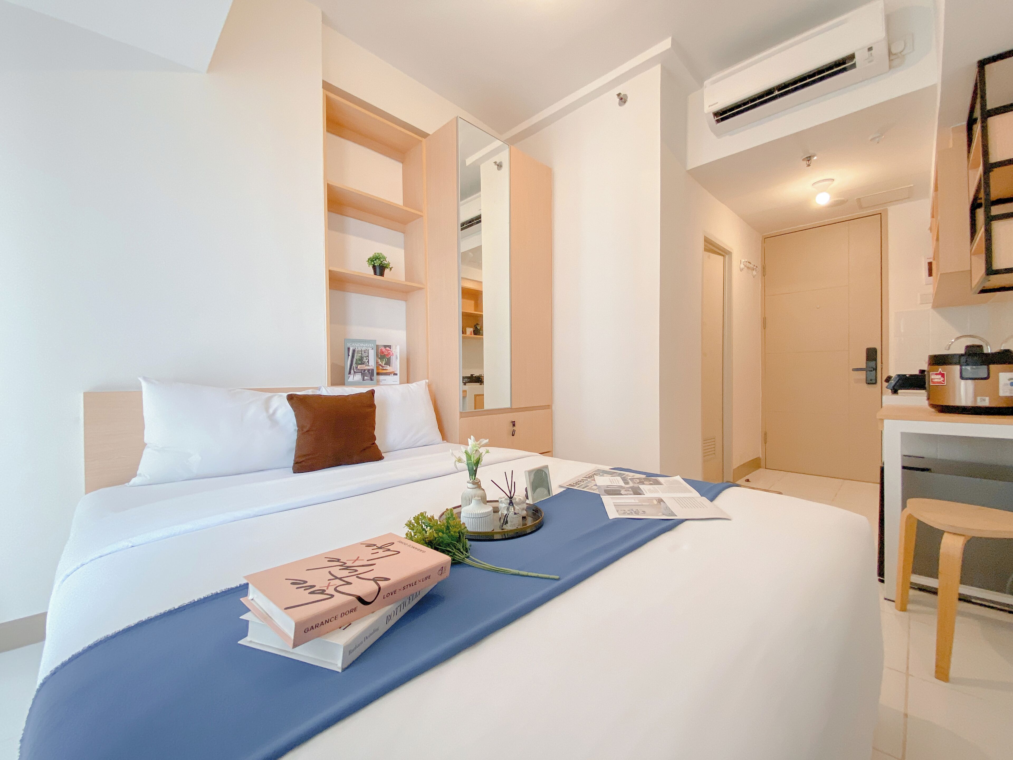 Una habitación de hotel moderna con una cama bien hecha, un escritorio con silla y una pequeña área de kitchenette.