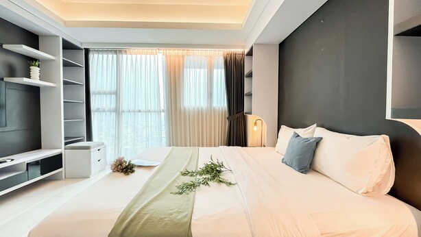 Una habitación de hotel moderna con una cama grande, un televisor en un estante y vistas de la ciudad a través de la ventana.