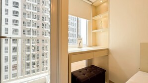 A modern bathroom with a large window, a vanity with a mirror, a shelf with a vase, and a brown bench.