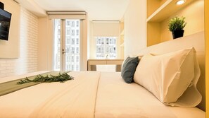 Une chambre d’hôtel avec un lit, une télévision, une fenêtre donnant sur d’autres immeubles et une plante posée sur une étagère.