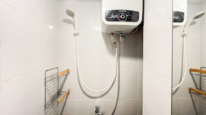 Une salle de bain avec des murs carrelés de carreaux blancs, une douche équipée d’un pommeau de douche à main, un panneau de commande fixé au mur et un porte-serviettes en métal doté de poignées en bois.